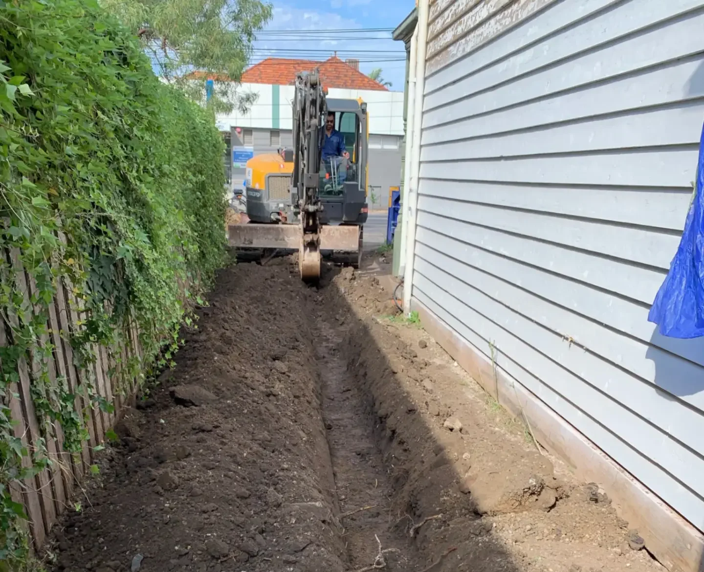 Mini excavator completing drainage trenching alongside residential property by Adaptive Green Space